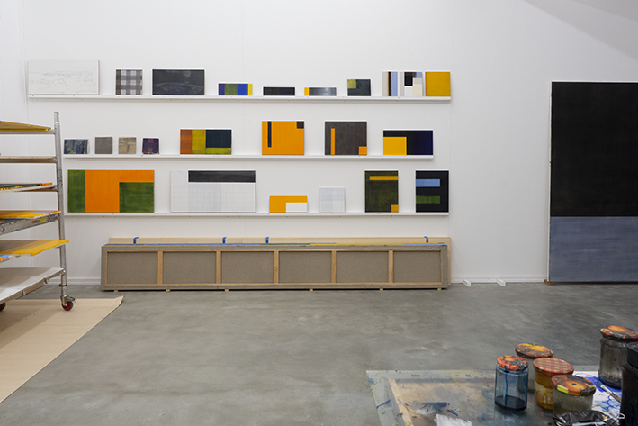 Atelier von Roger Schnyder in Doppleschwand. Weisse Wand, auf drei Regalen aufgereiht Malereien.